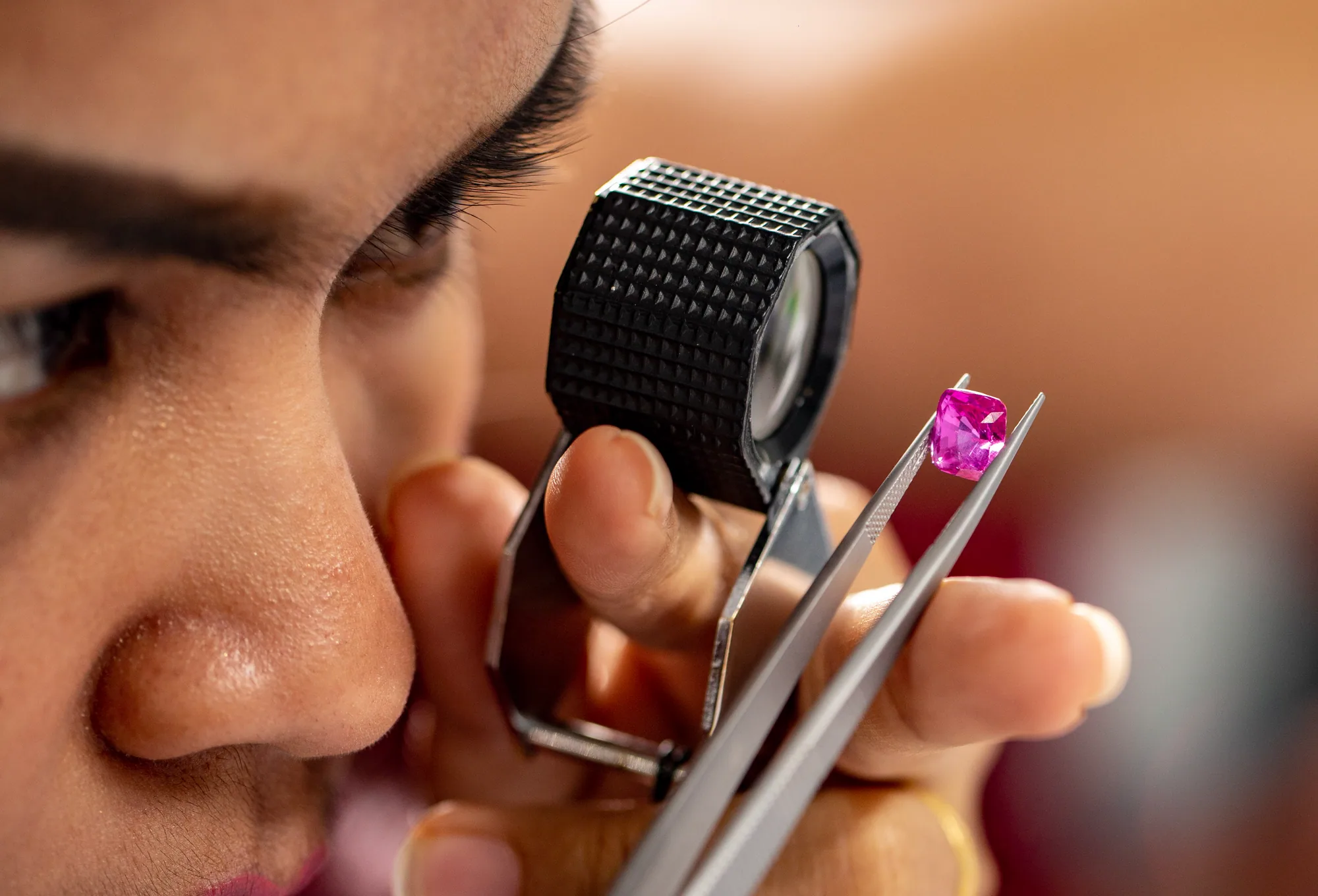 Gemologist inspecting a pink gemstone with a loupe